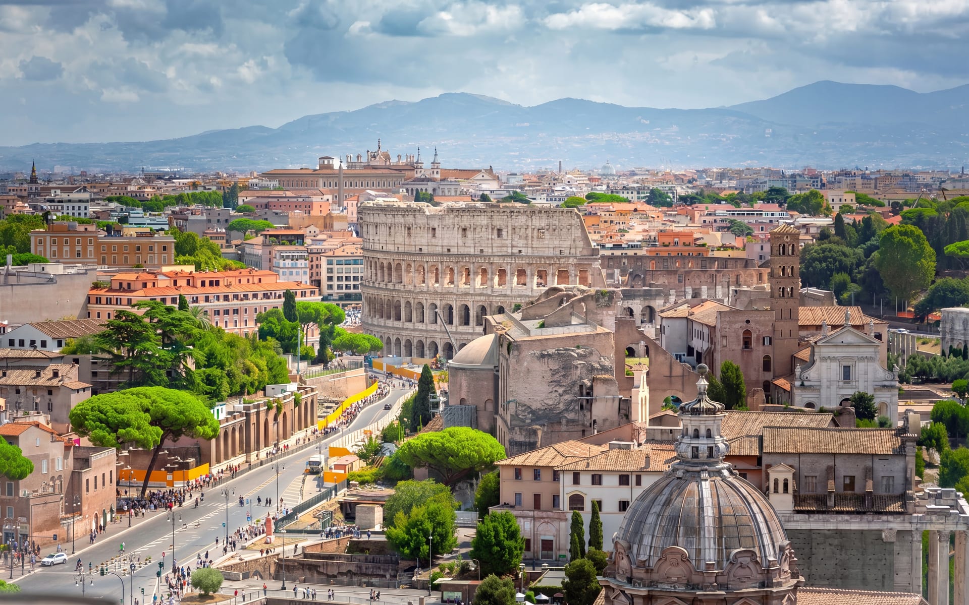 Veduta panoramica di Roma con il Colosseo e via dei Fori Imperiali, tra pini marittimi e cupole del centro storico